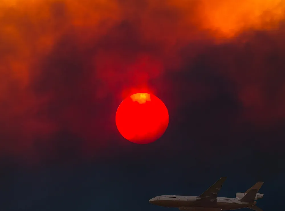 DC-10 air tanker flying low under a red sun in heavy wildfire smoke