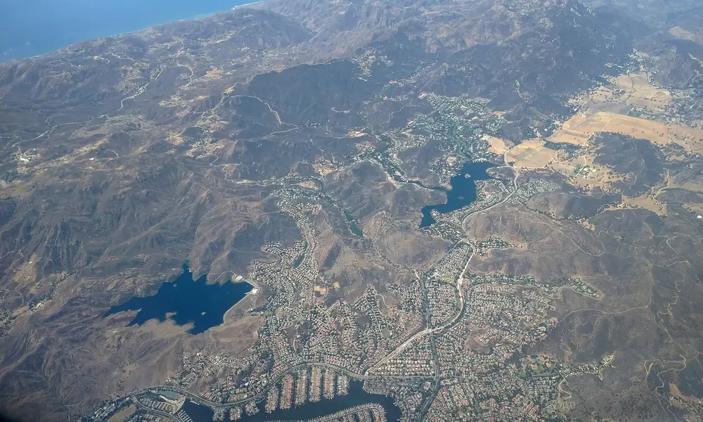 Aerial view of reservoirs and a small lake among dry hills, with the ocean on the horizon