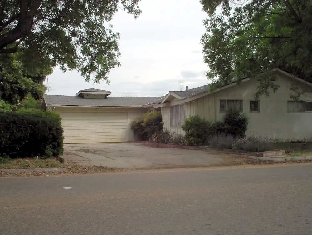 Single-story ranch house with a wide attached garage and a hedge along the drive