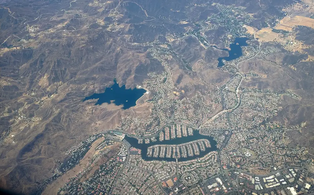 Aerial view of a loop-shaped lake ringed by homes, with hills and reservoirs beyond